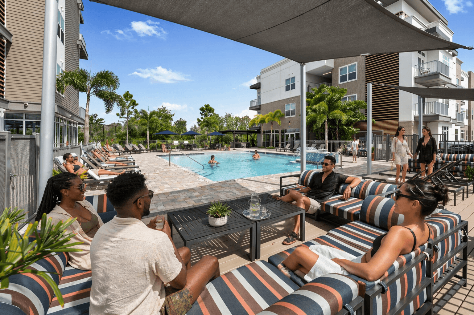 People are sitting on a striped couch by a pool.